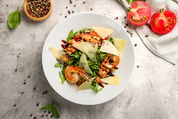 Arugula with shrimps and parmesan on plate on grey concrete table top view