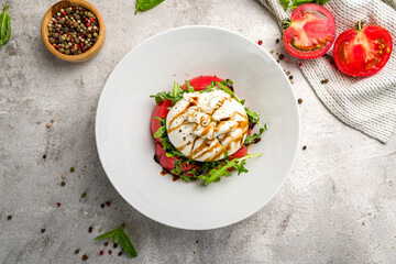 Salad with buratta cheese and tomatoes on plate on grey concrete table top view