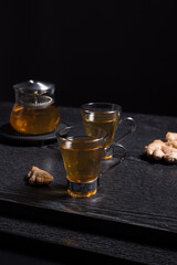 Dos tazas de té de jengibre con tetera sobre una mesa de madera negra
