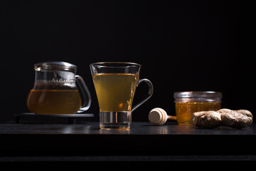 Una taza de té de jengibre con tetera y miel sobre una mesa de madera negra