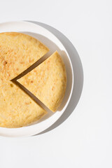 Tortilla de patatas española hecha con aceite de oliva, huevos y patatas en un plato blanco sobre una mesa blanca. Aperitivo español. Vista superior	