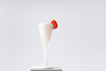 Copa de champán burbujeante derramado adornado con una fresa sobre fondo gris claro. Celebración	