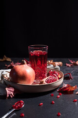 Jugo de granada con semillas y trozos de granada sobre fondo negro con hojas secas de otoño	