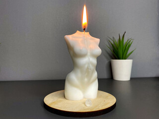 Candle in woman torso shape burning in grey modern interior room, atmosphere and smoke after candle