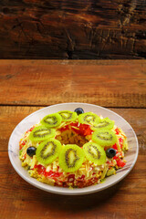Puff salad with chicken breast, garnished with kivi and olives in a salad bowl on a wooden table.
