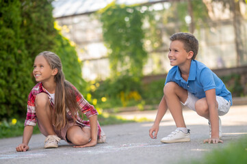 Joyous children drawing with colored chalks on the ground