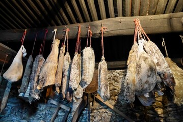 Corsican sausage specialities hanging from wooden beam in traditional stone cellar. Saucisson,...