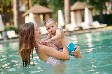 Fototapeta na wymiar Young pretty woman in a swimming pool with her baby boy