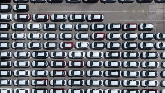 Top down aerial view of parking lot filled with brand new cars waiting for sale and transportation. Flying over large parking area at shipping docks, automobile industry.