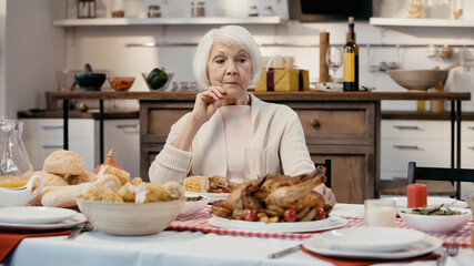 thoughtful senior woman sitting alone at table served with thanksgiving dinner in kitchen.