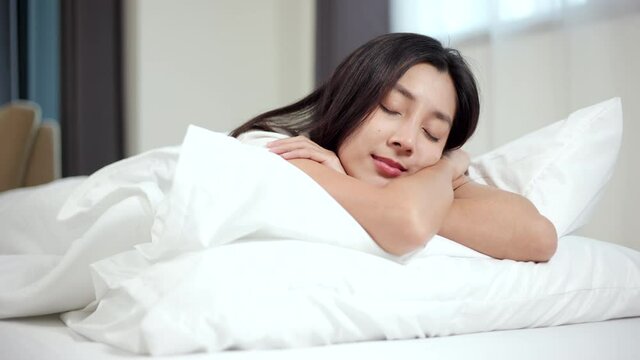 Beautiful asian woman make a bed to prepare lying asleep enjoying healthy good sleep nap in the morning. Young woman sleeping well in comfortable cozy fresh bed on soft pillow white linen.  