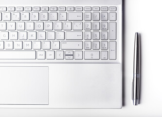 Laptop keyboard and pen of silver color, top view. Business and technology concept.