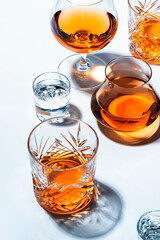 Strong alcoholic drinks, hard liquors, spirits and distillates in glasses: vodka, cognac, whiskey and other. White background. Hard light, copy space
