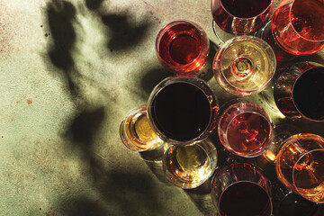 Red, white and rose wines in assortment in glasses on green background, top view. Wine bar, shop, winery, wine tasting concept. Hard light and harsh plant shadows