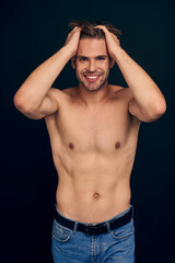 Handsome young bearded man isolated. Topless muscular man in jeans posing on dark blue background. Serious man looking at camera