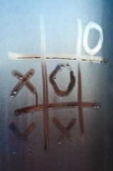 The concept of loneliness during the coronavirus pandemic. Tic-tac-toe is painted on the misted glass.