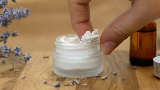 Woman takes a white cream from a glass jar with her finger. The concept of beauty and health and skincare for the body, face, and feet. Macro. Close-up
