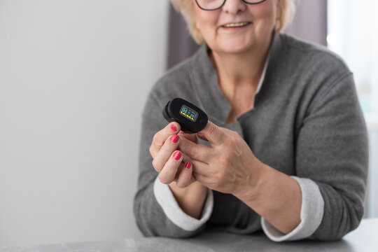 Smiling senior woman using pulse oximeter at home, measuring oxygen saturation by herself, pulse rate check-up of, controls health indicators during pandemic period. Healthcare and medicine concept