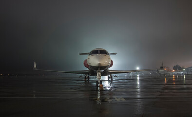 Twin-engine jet business jet parked on wet asphalt airport parking lot at night - Powered by Adobe