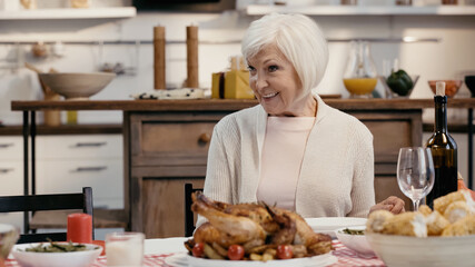 Obraz na płótnie Canvas happy senior woman sitting near roasted turkey and red wine during thanksgiving dinner.