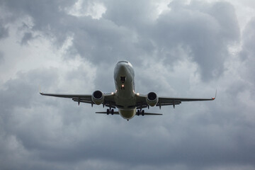 A passenger jet airliner is landing agaist clousy sky