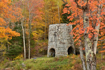 Colorful fall foliage and ruins of 19th century stone furnace for melting iron ore used to make...