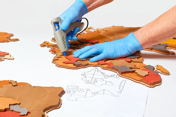A man glues a wooden model of the country to the world map in Russian using a glue gun.