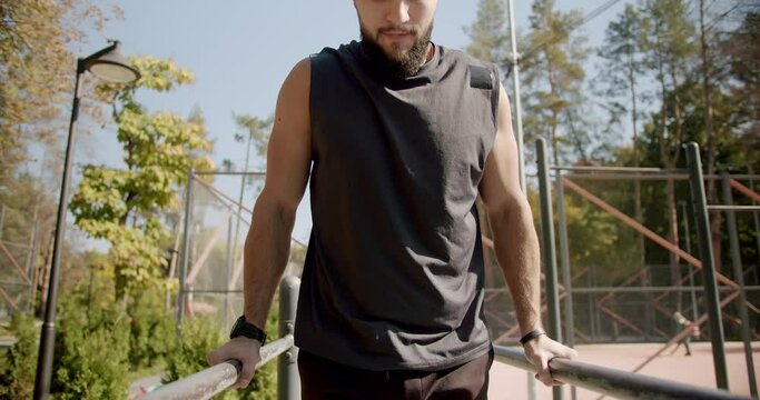 Muscular man doing push ups exercises on parallel bars, ABS, workout outdoors