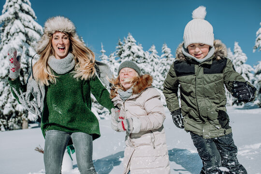 Mother with 2 laughing children in the snowy winter landscape romps in the snow and makes a snowball fight.