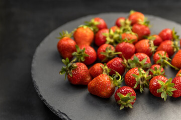 Freshly picked farmers organic strawberries on gray platter. Ripe strawberries with green cuttings.
