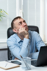 Naklejka premium Brooding young man in the office behind the workplace. Portrait of an office manager. Male Secretary. Vertical frame