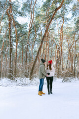 Fototapeta na wymiar Young couple of lovers stands in the winter forest and looks at each other. People Outdoors. Vertical frame