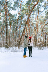 Young couple of lovers stands in the winter forest and looks at each other. People Outdoors. Vertical frame