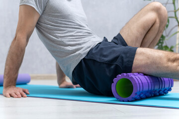 Man sits on yoga mat and doing massage his feet with foam roller. Workout at home. Roller for...