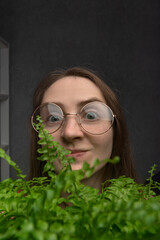 Cheerful girl with glasses holds green houseplant. Close-up portrait of young woman with...
