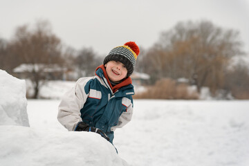 Fototapeta na wymiar Cheerful child boy in knitted hat builds snow fortress in winter. Winter holidays.