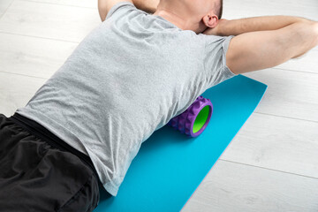 Man lies on the myofascial roller. Man performs myofascial release of hyper-movable back muscles...