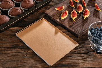 Blank notepad for notes on a wooden table. Chocolate muffins and sliced figs on background