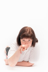 Young woman lies on the floor and shows Look into my eyes sign. Portrait of dark-haired girl on white background.