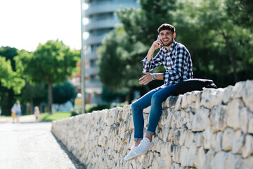 Obraz premium Handsome, smiling young man sitting on a stone wall using his cell phone