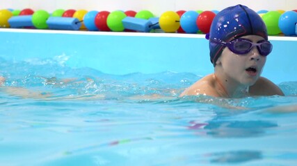 Close up portrait of young Caucasian boy swim in pool with blue water, hold swimming board. Indoor. Slow motion. Concept of active leisure.