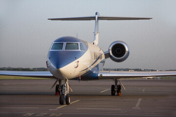 A twin-engine business jet plane stands at the airport in the parking lot at summer 