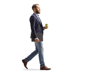 Full length profile shot of a young professional man walking with a takeaway coffee cup and a laptop