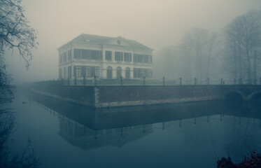 spooky eerie building and reflection of water in the mist at Schoonselhof