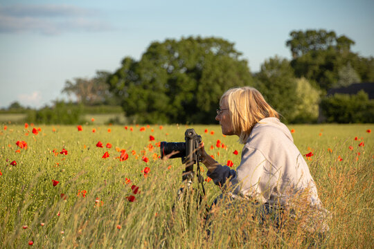 woman photographer taking photos with tripod in poppy field in England
