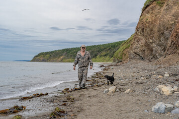 An elderly man walks with a dog along the seashore
