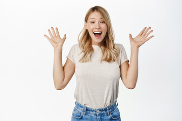 Fototapeta na wymiar Surprised and excited blond girl screams of joy, reacting amazed and happy at promo sale, super big news, standing over white background