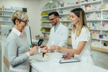 Fototapeta premium Two pharmacist giving prescription medications to senior female customer in a pharmacy