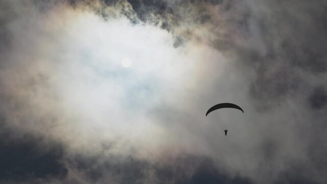 Paragliding adventure sport against bright sun on cloudy sky