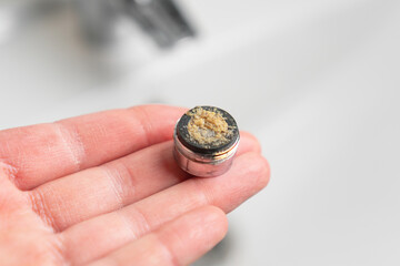 Clogged filter aerator of bathroom sink faucet on a plumbers hand with calcium sediment. Cleaning...